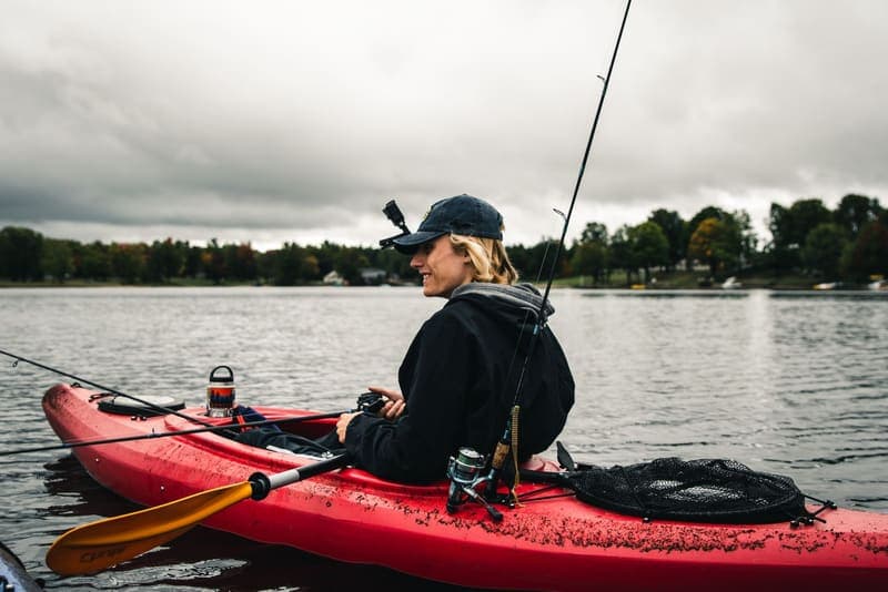A person fishing from a kayak on a lake under overcast skies