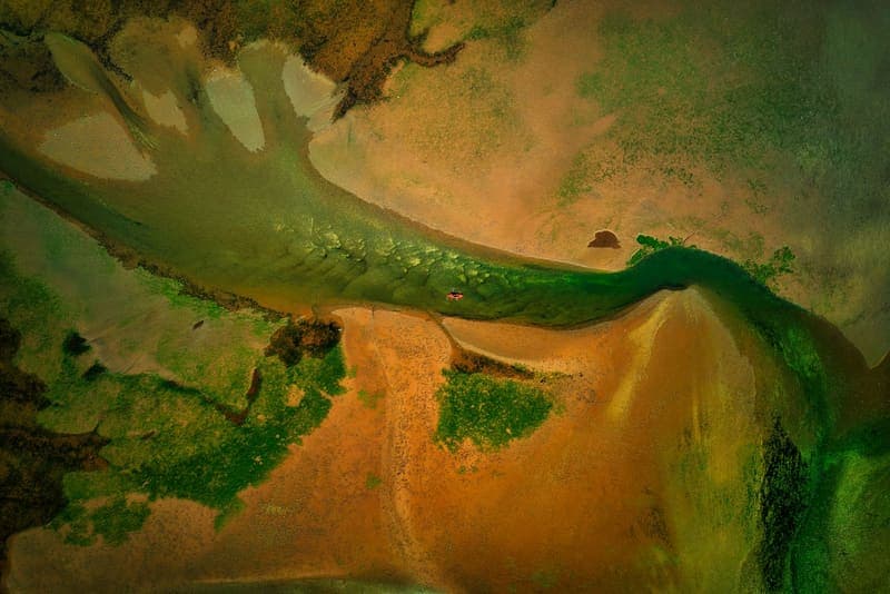 A kayaker paddling across shallow estuary water seen from above
