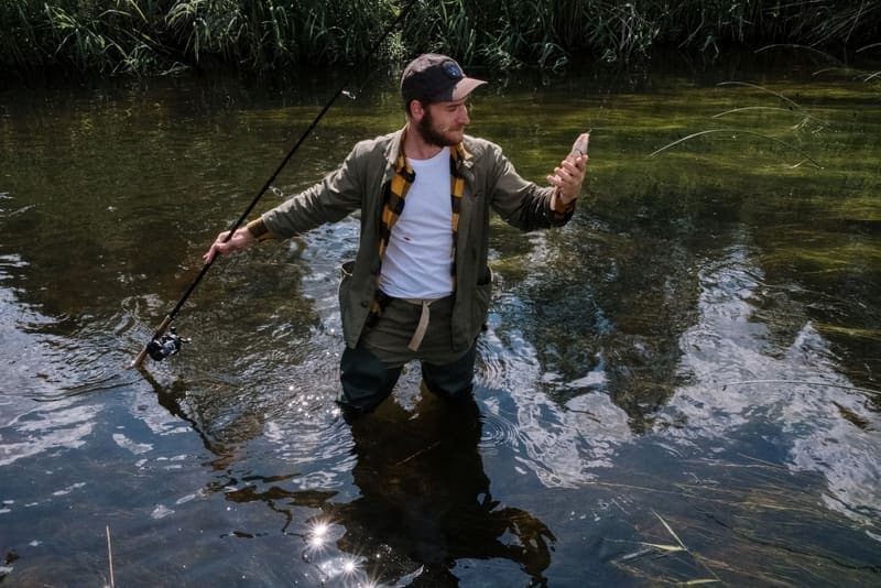 An angler standing in a river holding a rod and a smartphone