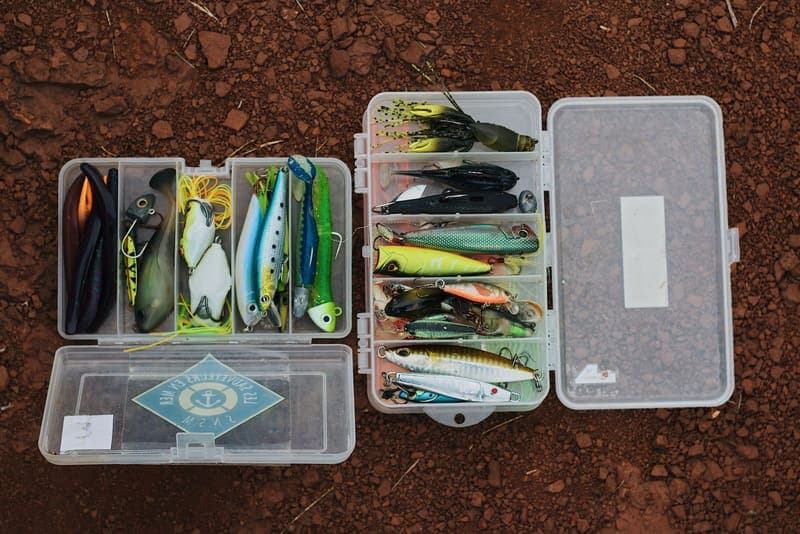 Open tackle boxes with colorful fishing lures laid out on rock