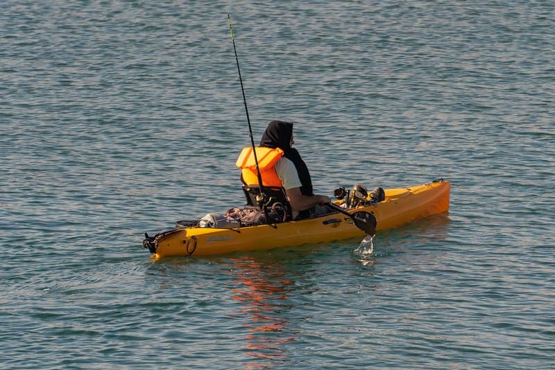 A man fishing from a kayak on a calm lake
