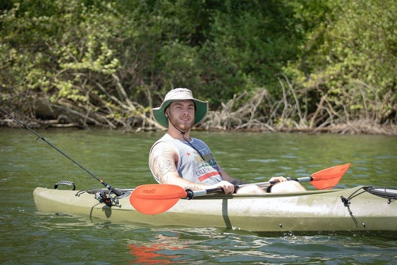 A man in a hat sitting upright in a kayak on a sunny river