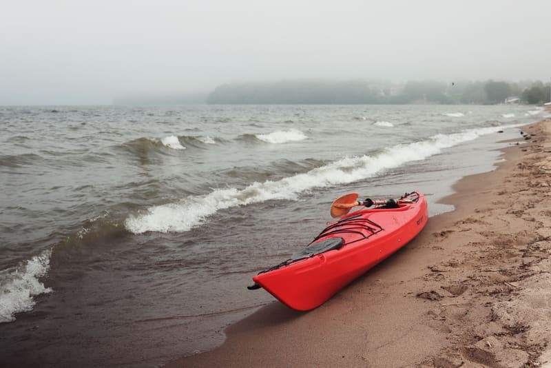 A red kayak on a misty beach at the water's edge
