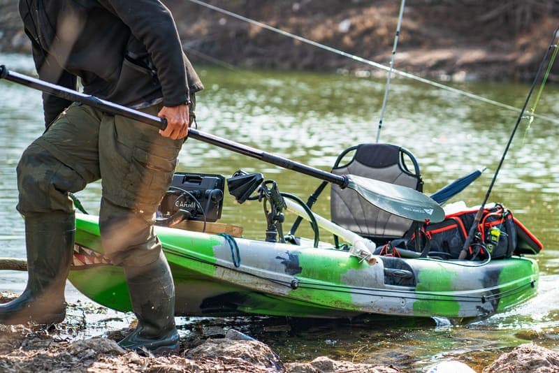 A rigged fishing kayak at the water's edge with a fish finder, rod and seat mounted on deck