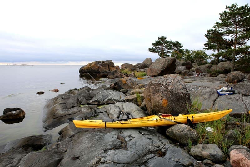 A yellow sea kayak resting hull-down on bare rock at a rocky landing