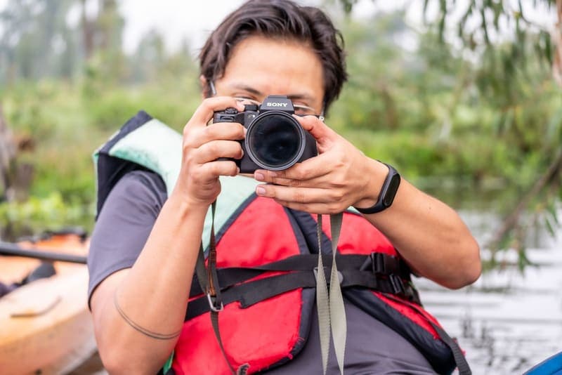 A paddler taking photographs from a kayak, wearing a life jacket