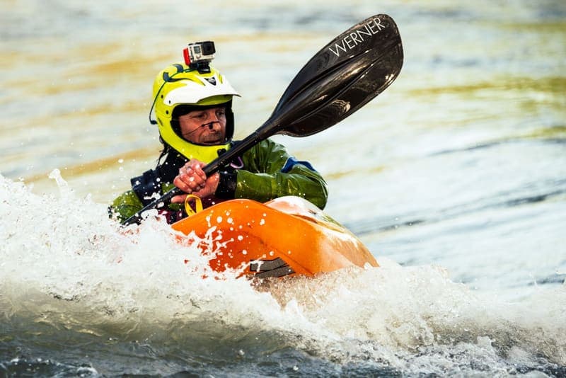 A kayaker in a sit-in boat with a sealed spray skirt as water breaks over the deck