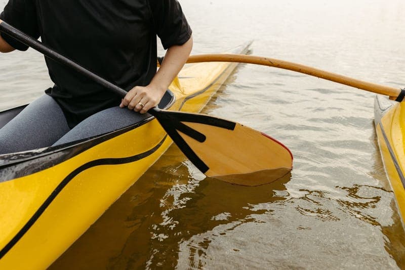 A paddler in a yellow outrigger canoe with the float and arm resting on flat water