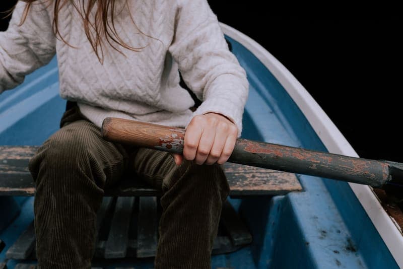 A paddler's hands holding a wooden paddle shaft in a small boat