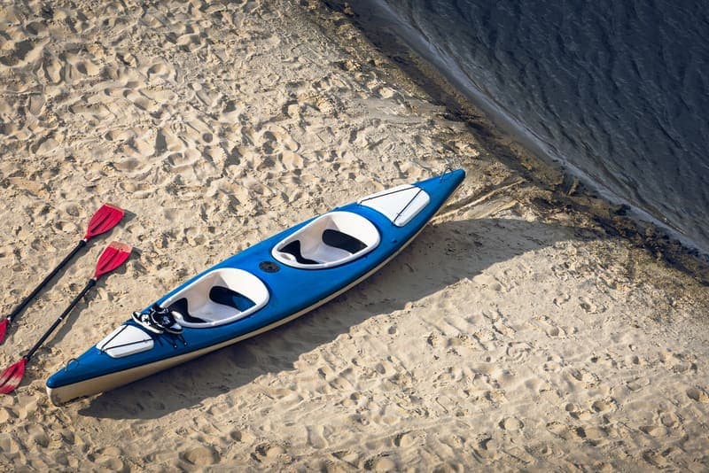 A blue kayak and two red paddles resting on a sandy beach