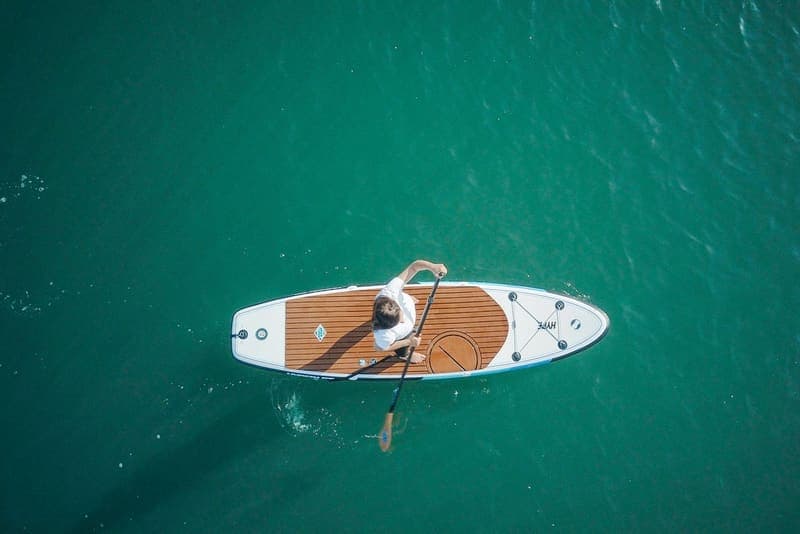 An adult paddleboarding on calm turquoise water, seen from above