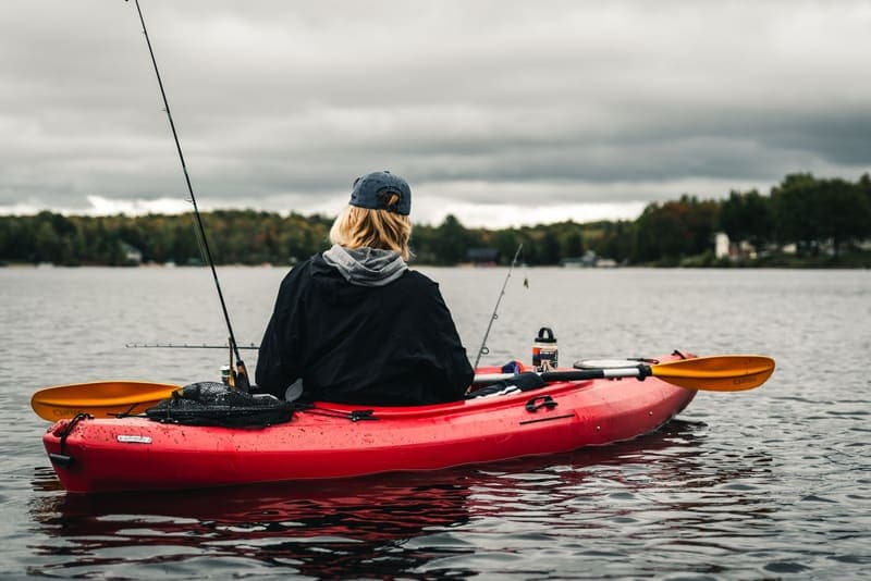 A person fishing from a red kayak on a calm lake, seen from behind