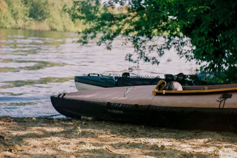 Kayaks resting on a riverbank under trees