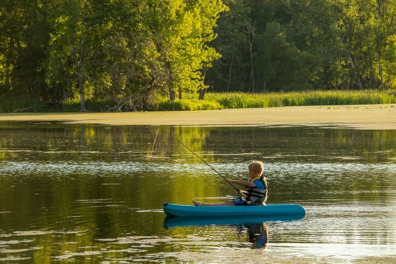 A young boy paddling a kayak and fishing on a calm lake