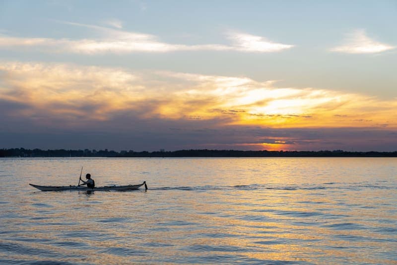 A lone kayaker paddling across calm open water at sunset