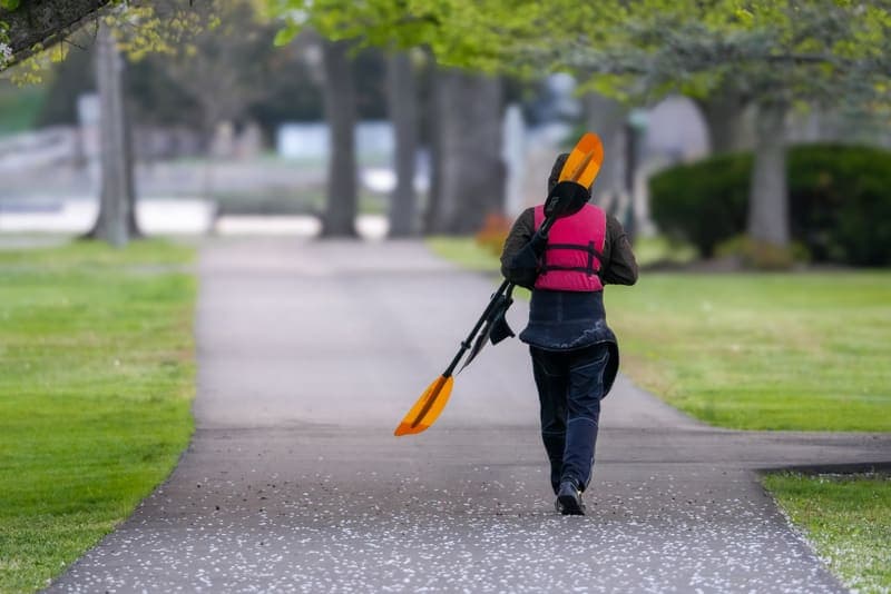A paddler wearing a life jacket carrying kayak paddles