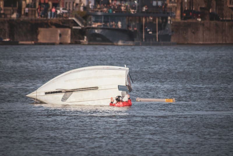 A capsized boat in open water with a person in a life jacket alongside