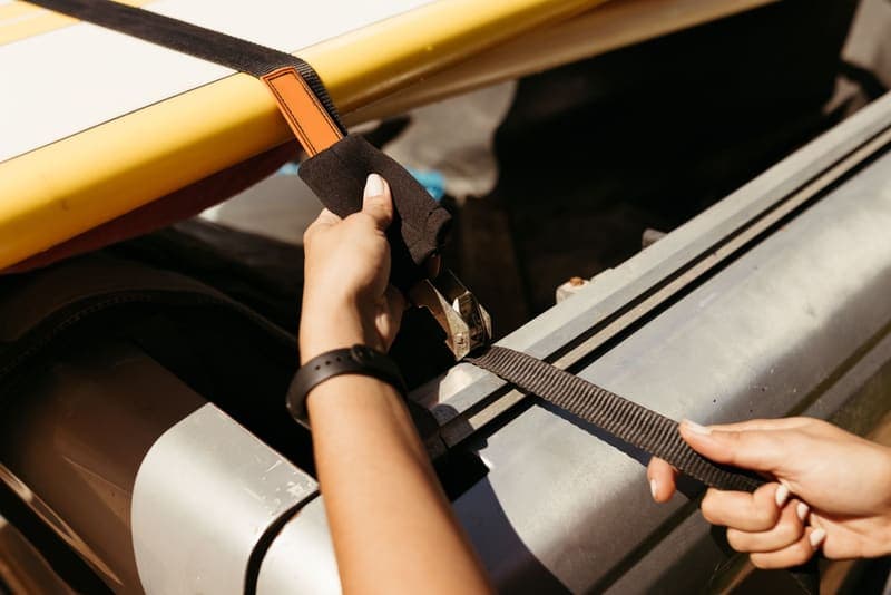 Hands tightening a strap over a boat on a vehicle roof