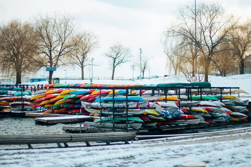 Kayaks stacked outdoors by a snowy waterfront in winter