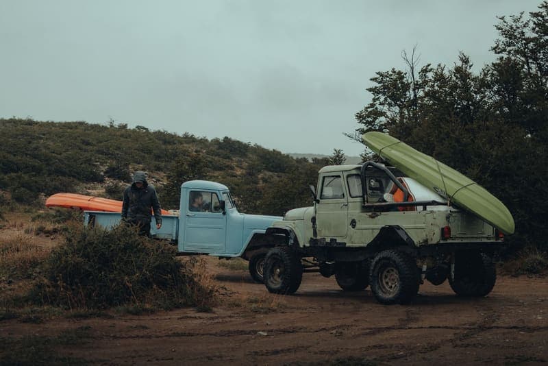 Two pickup trucks on a dirt trail, one with a kayak on a rack and one with a kayak in the bed