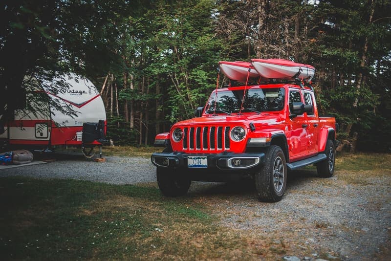 Two kayaks carried side by side on the roof rack of a red truck at a campsite